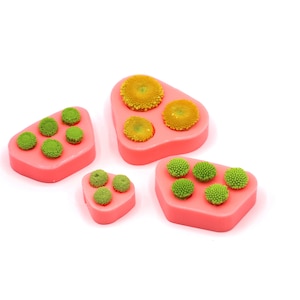 Op de afbeelding: Vier roze siliconen mallen voor het maken van bloemvormige decoraties. De mallen zijn in verschillende maten en vormen, en elk heeft een ander aantal bloemvormige holtes. De mallen zijn gevuld met kleine groene en gele bloemen.