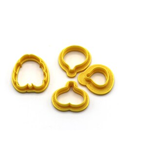 Puede incluir: Cuatro cortadores de galletas de plástico amarillo en forma de flor, pera, corazón y círculo.