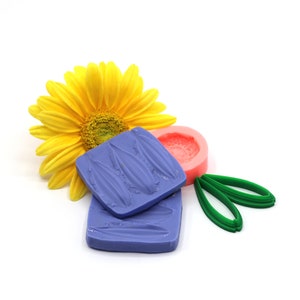 Könnte beinhalten: Zwei lila Silikonformen zum Backen, eine mit einem Blattdesign und die andere mit einem Wellenmuster. Eine rosa Silikonform mit einem Blumendesign und eine grüne Silikonform mit einem Blattdesign sind ebenfalls enthalten.