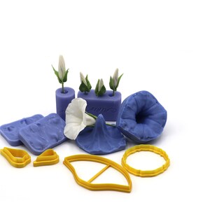 May include: A set of blue silicone molds for making polymer clay flowers. The molds include a trumpet-shaped flower, a bud, and a leaf. There are also yellow plastic cutters for making flower petals and leaves.