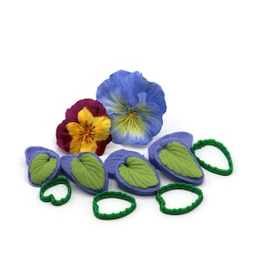 May include: A set of silicone moulds for making fondant flowers. The set includes three leaf moulds and two flower moulds. The flower moulds are blue, purple, and yellow. The leaf moulds are green.