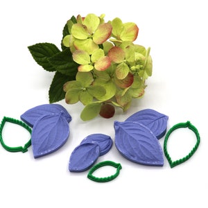 Op de afbeelding: Een set groene plastic bladstempels en paarse siliconen bladvormen voor het maken van fondant- of gum paste-decoraties.