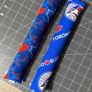 May include: Two blue cat toys. One has a pattern of red and white maple leaves on a blue background. The other has the Toronto Blue Jays logo and text. Both are cylindrical and made of fabric.