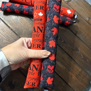 May include: Cat toys with Canadian designs. One is red with maple syrup and poutine text, another is black with red maple leaves. The toys are long and cylindrical, with the text "eh?" on one.