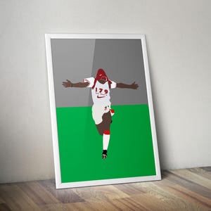 Pode incluir: Uma impressão emoldurada com uma ilustração estilizada de uma pessoa em uniforme esportivo branco e vermelho com os braços estendidos. A figura corre em um campo verde contra um fundo cinza. A impressão tem uma borda branca.