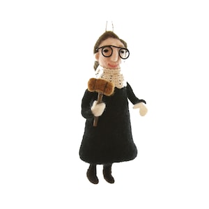 May include: A felt ornament depicting a person wearing a black robe and glasses, holding a gavel. The ornament is brown, black, and white.
