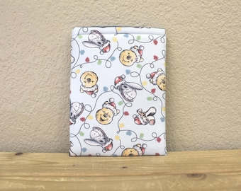 May include: White fabric pouch with a Christmas-themed print featuring Winnie the Pooh and Tigger wearing Santa hats. The print also includes a string of lights and presents.