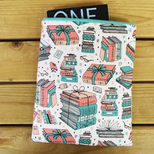 May include: A white book sleeve with a pattern of stacked books, wrapped gifts, and eyeglasses in teal, coral, and black. The sleeve has a teal border and holds a book with the word "ONE" visible.