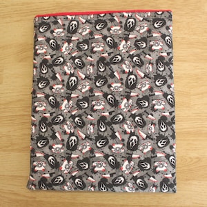 May include: A gray fabric book cover with a red trim. The cover features a repeating pattern of black and white Scream masks, old-fashioned telephones, and bloody knives. The design is set against a backdrop of black splatters.