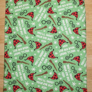 May include: A green fabric item with a repeating pattern of red and black plaid hats, eyeglasses, rifles, and snowflakes. The text "YOU'LL SHOOT YOUR EYE OUT, KID!" is also printed on the fabric.