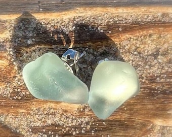 Puede incluir: Dos piezas de vidrio de mar, una verde claro y otra verde pálido, con un cierre de pendiente de plata unido a una de las piezas.