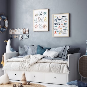 May include: A white daybed with a white and blue striped blanket and pillows. Two framed posters hang on the wall behind the daybed. One poster features a colorful illustration of sea creatures and the other poster features a colorful illustration of sea creatures and numbers.
