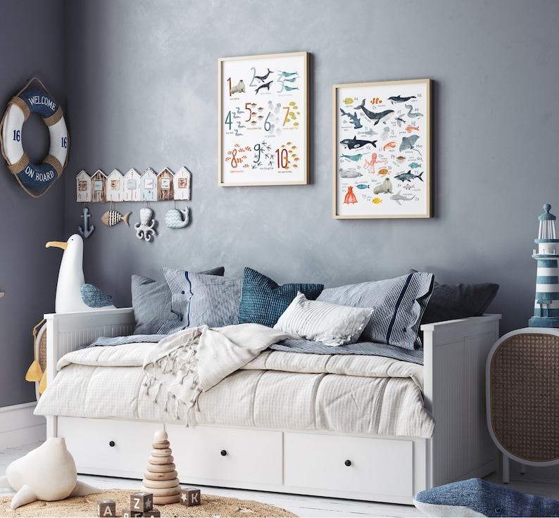 May include: A white daybed with a white and blue striped blanket and pillows. Two framed posters hang on the wall behind the daybed. One poster features a colorful illustration of sea creatures and the other poster features a colorful illustration of sea creatures and numbers.