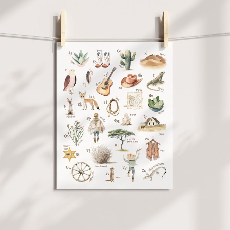 May include: Watercolor alphabet poster featuring Western-themed illustrations. Includes images of boots, a guitar, a cactus, a lizard, a sheriff's star, and a tumbleweed. The poster is hanging from a clothesline with wooden clips.