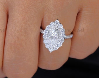 May include: A close-up of a hand wearing a silver ring with a large oval-shaped diamond surrounded by smaller diamonds. The ring is set in a halo style.