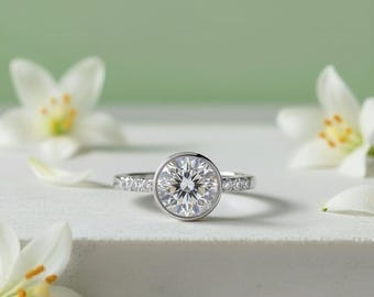 May include: A silver-toned ring featuring a large, round, faceted center stone set in a smooth bezel. The band is accented with a row of small, clear, round-cut stones on each side, creating a bright, reflective appearance against the metal.