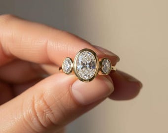 Anello a tre pietre con diamanti ovali creati in laboratorio e incastonati a castone: fede nuziale trilogy in oro giallo 14 carati.