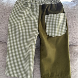 Könnte beinhalten: Hose mit grün-weißem Vichy-Muster mit einem olivgrünen Einsatz und einer Tasche. Die Hose hat einen elastischen Bund. Die Tasche ist ebenfalls kariert. Die Hose ist aus einem weichen Stoff gefertigt.