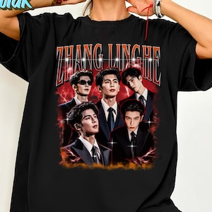 May include: Black oversized t-shirt featuring a graphic of five men in suits with the text "ZHANG LINGHE" in orange and white. The design has a vintage, distressed look with a red and orange background.