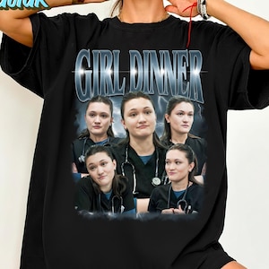 Könnte beinhalten: Schwarzes T-Shirt mit dem Text "GIRL DINNER" in einer silbernen, stilisierten Schrift. Das Shirt zeigt eine Collage von Bildern einer Person, die ein schwarzes Oberteil und ein Stethoskop trägt. Das Shirt hat einen Rundhalsausschnitt.