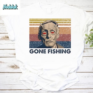 Könnte beinhalten: Ein weißes T-Shirt mit einer Grafik im Vintage-Stil eines Mannes mit roten Augen und Hörnern, einem Kreuz auf der Stirn und dem Text "GONE FISHING".