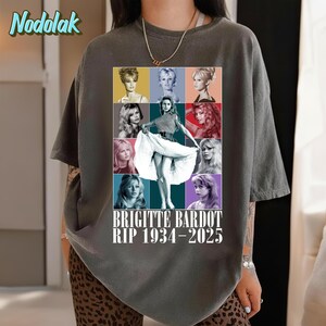 K&ouml;nnte beinhalten: Dunkelgraues T-Shirt mit einer Collage von Bildern von Brigitte Bardot. Das zentrale Bild zeigt Bardot in einem wei&szlig;en Kleid, umgeben von anderen Portr&auml;ts. Der Text "BRIGITTE BARDOT RIP 1934-2025" ist darunter gedruckt.