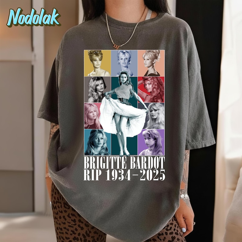 K&ouml;nnte beinhalten: Dunkelgraues T-Shirt mit einer Collage von Bildern von Brigitte Bardot. Das zentrale Bild zeigt Bardot in einem wei&szlig;en Kleid, umgeben von anderen Portr&auml;ts. Der Text "BRIGITTE BARDOT RIP 1934-2025" ist darunter gedruckt.