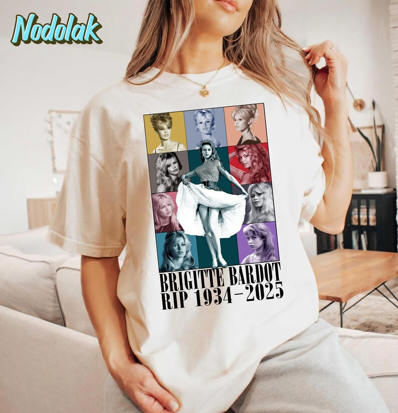 K&ouml;nnte beinhalten: Cremefarbenes T-Shirt mit einem farbenfrohen Grafik von Brigitte Bardot. Die Grafik enth&auml;lt mehrere Bilder der Schauspielerin und den Text "BRIGITTE BARDOT RIP 1934-2025". Das Shirt hat kurze &Auml;rmel und einen Rundhalsausschnitt.