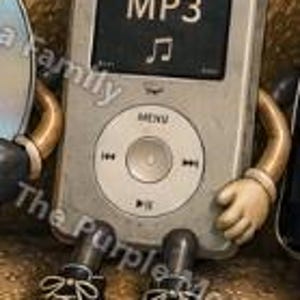 May include: A silver digital music player with a rectangular screen displaying the text MP3 and a musical note icon. The device features a circular navigation wheel with menu and playback controls, attached to tan arms and black lace-up sneakers.