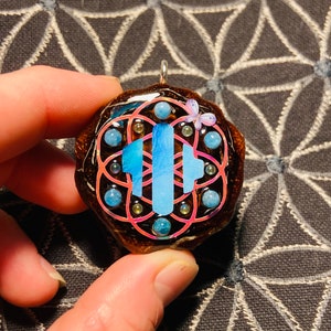 May include: A brown resin pendant with a blue and pink geometric design, surrounded by small blue stones and a pink butterfly charm.