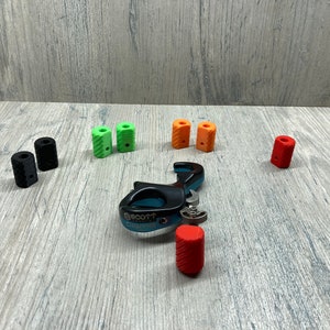 May include: A blue and black archery release aid with a variety of colored nocks. The nocks are in black, green, orange, and red.