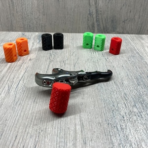 May include: A set of colorful rubber grips for a bow release aid. The grips are in red, orange, black, and green. The release aid is made of metal and has a black handle.