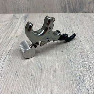 May include: Silver archery release aid with a black trigger and a silver knob. The release aid has the text "STAN" and "PRO" printed on it.