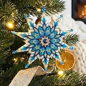 May include: A detailed, beaded snowflake decoration in blue, white, and gold hangs on a Christmas tree. The tree is adorned with lights and dried orange slices. The background features a fireplace and a cosy blanket. The ornament is star-shaped and intricately designed.