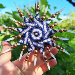 Könnte beinhalten: Nahaufnahme eines perlenbesetzten Stern-Anhängers mit einem blau-weißen Muster. Der Stern hängt an einer Schnur und wird in einer Hand gehalten. Der Text "Crazy ribbon 24PS2D005 - 36/10 and 56/15 rows" ist am unteren Rand des Bildes sichtbar.