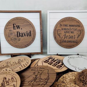 Może przedstawiać: Kolekcja drewnianych tabliczek z różnymi powiedzeniami i wzorami. Tabliczki są okrągłe i mają rustykalny wygląd. Niektóre z powiedzeń to "Ew, David", "Rano, gdy wstaję, daj mi Jezusa (i kawę)", "Wszystko o tej bazie" i "Życie jest lepsze z psem".