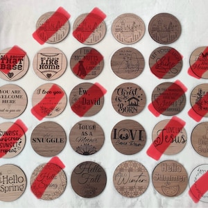 Może przedstawiać: Zbiór 24 okrągłych podkładek pod kubki wykonanych z drewna z różnymi wzorami i powiedzeniami. Podkładki przedstawiają różne motywy, w tym sport, święta i inspirujące cytaty. Niektóre z powiedzeń to "All About That Base", "No Place Like Home", "I Like Big Mutts", "Let Your Light Shine", "Faith Can Move Mountains", "You Are Welcome Here", "I Love You", "Ew David", "Christ Is Born", "In The Morning When I Pray Give Me Jesus And Coffee", "He Is Not Here He Is Risen", "Sunrise Sunscreen Sunset Repeat", "Let's Snuggle", "Tough As A Mother", "Love Comes Down", "Love Like Jesus", "Hoppy Easter", "Hello Spring", "Hello Spring", "Hello Fall", "Hello Winter", "Hello Summer", "Days Not To Be Missed".