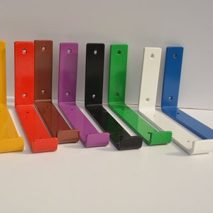 Puede incluir: Diez soportes de estantería de metal en varios colores, incluyendo amarillo, rojo, marrón, morado, negro, verde, blanco y azul. Los soportes son todos del mismo tamaño y forma, y están dispuestos en una fila sobre una superficie blanca.