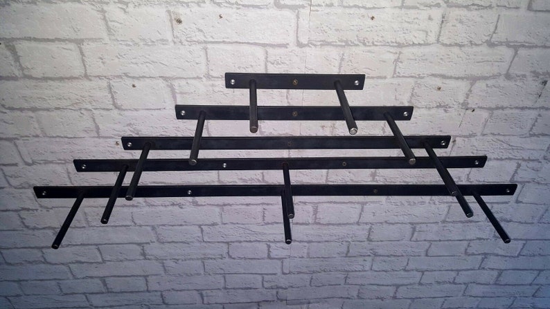 May include: Five black metal shelf brackets mounted on a white brick wall. The brackets are arranged in a staggered pattern, with the longest bracket at the bottom and the shortest bracket at the top.
