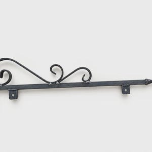 May include: A black metal wall-mounted bracket featuring a horizontal arm with a pointed finial at the end. The structure includes a vertical mounting plate and decorative scrollwork along the top, with two small hanging loops attached.