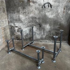 May include: Galvanised steel pipe table base, featuring a minimalist industrial design. The base is constructed from horizontal and vertical pipes, connected by elbows and flanges. The table base is ready for a tabletop, and is suitable for a variety of uses.