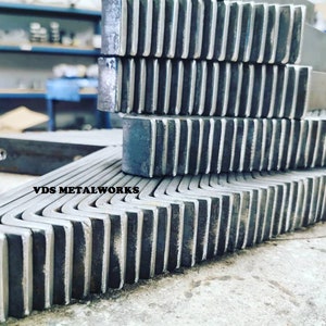 Op de afbeelding: Een stapel metalen hoekbeugels met een gekartelde rand. De beugels zijn gemaakt van staal en hebben een zilveren afwerking. De tekst "VDS METALWORKS" is zichtbaar op de onderste beugel.
