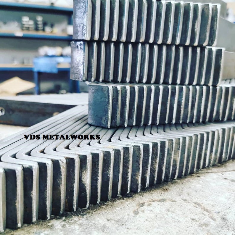 Op de afbeelding: Een stapel metalen hoekbeugels met een gekartelde rand. De beugels zijn gemaakt van staal en hebben een zilveren afwerking. De tekst "VDS METALWORKS" is zichtbaar op de onderste beugel.