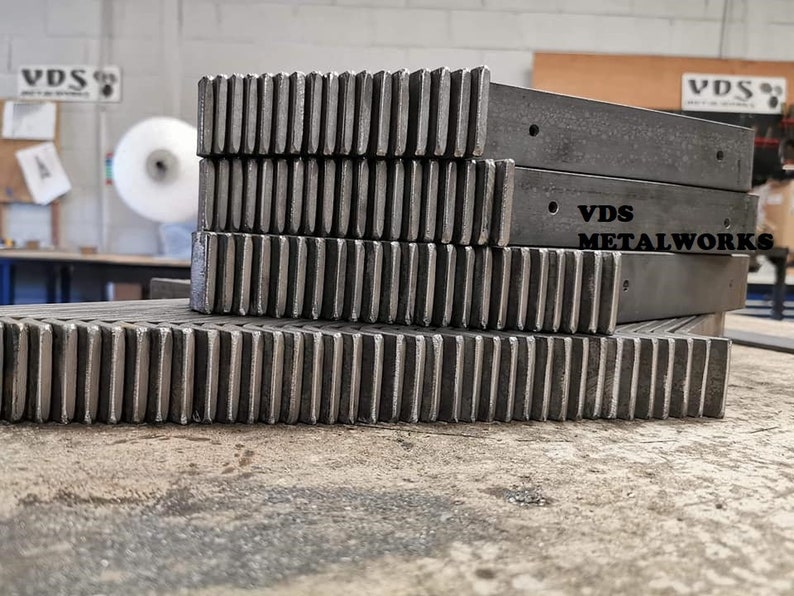 Op de afbeelding: Een stapel metalen tandwielen met een VDS Metalworks-logo op het bovenste stuk. De tandwielen zijn gemaakt van donkergrijs metaal en hebben een ruwe, industri&euml;le uitstraling.
