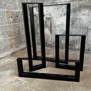 May include: Four black metal table legs in different sizes, stacked on top of each other. The legs are made of square tubing and have a black powder coat finish.