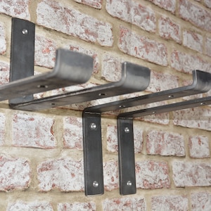 Puede incluir: Cuatro soportes de estanter&iacute;a de metal montados en una pared de ladrillo. Los soportes est&aacute;n hechos de metal resistente y tienen un aspecto r&uacute;stico e industrial.