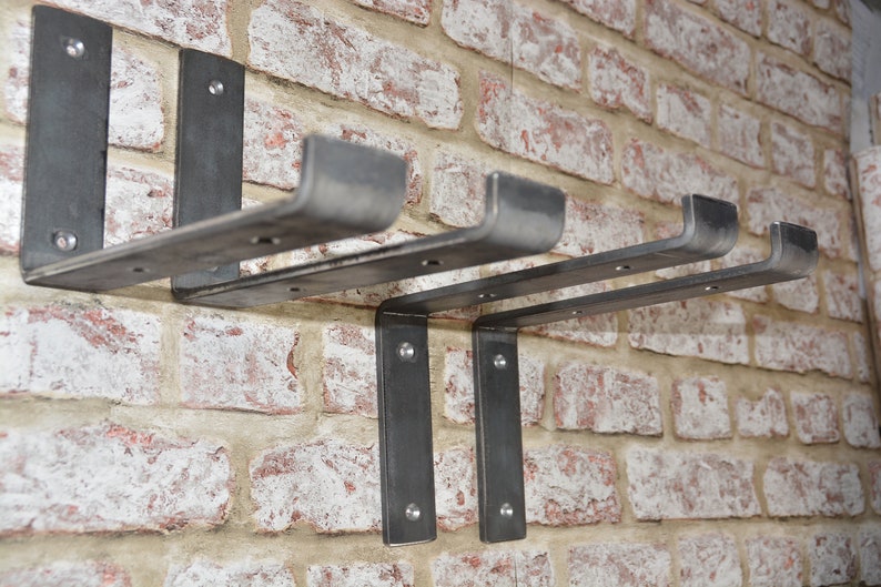 Puede incluir: Cuatro soportes de estanter&iacute;a de metal montados en una pared de ladrillo. Los soportes est&aacute;n hechos de metal resistente y tienen un aspecto r&uacute;stico e industrial.