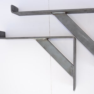 May include: Two metal shelf brackets, each with a 90-degree angle and a flat surface for mounting. The brackets are made of a light gray metal and are designed to support shelves.