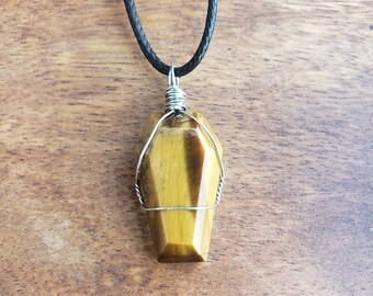 May include: A gold tiger's eye gemstone pendant wrapped in silver wire, hanging from a black cord necklace.