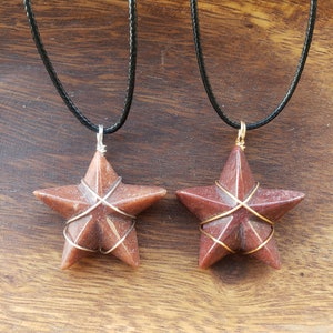 May include: Two red star-shaped pendants on black cords. The stars are wrapped with gold wire and have a speckled texture.